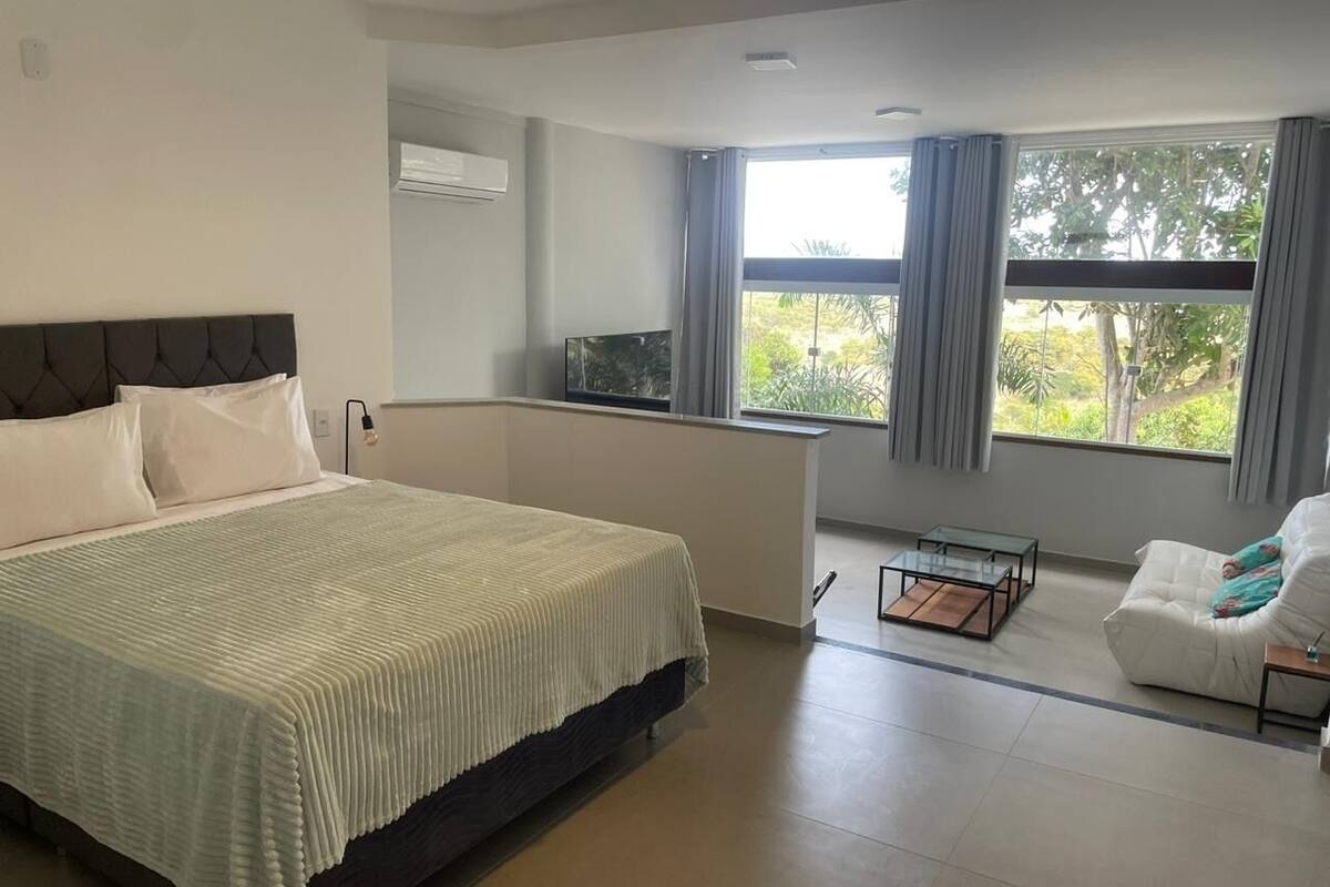 A modern bedroom with a large bed, a sofa, a TV, and a window with curtains.