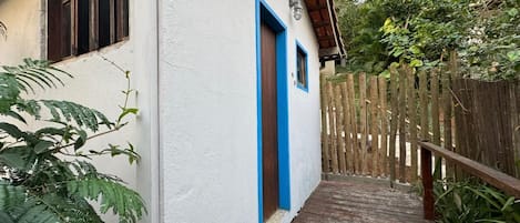 Um edifício branco com porta e molduras de janela azuis, um deck de madeira e uma cerca de madeira.