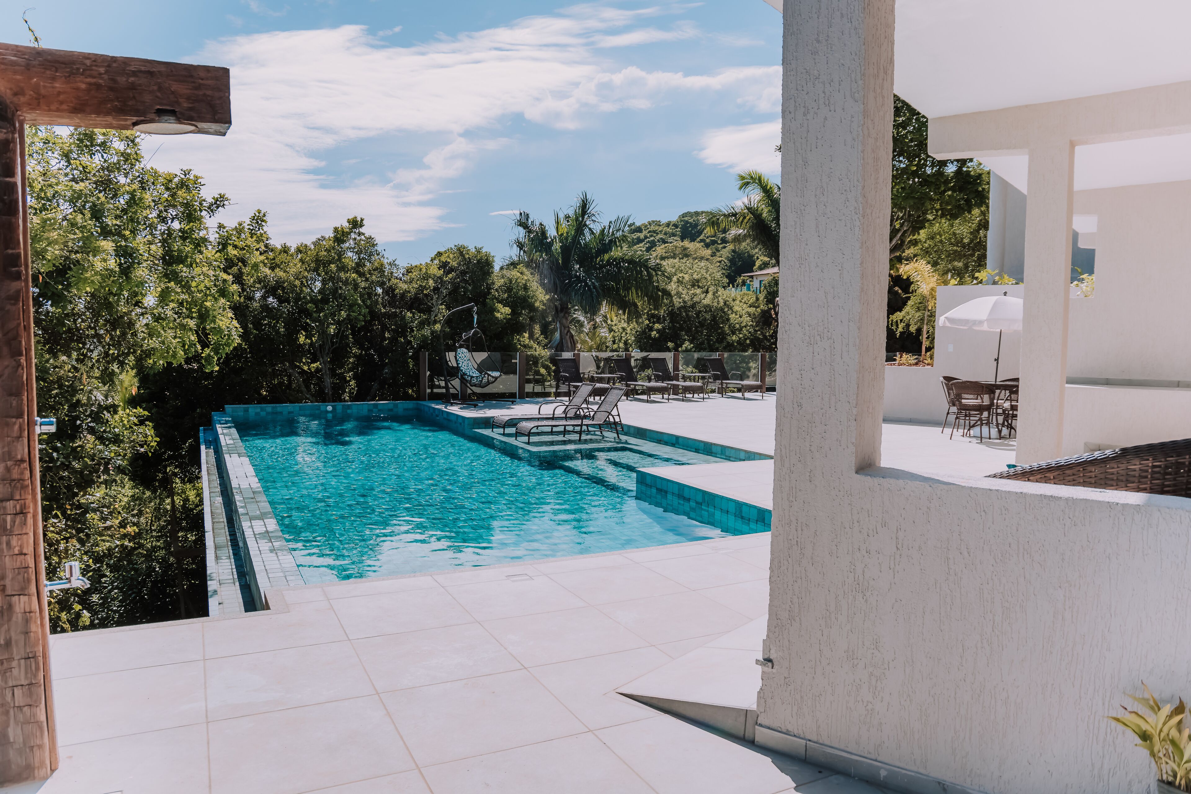 Piscina con sillas de descanso y una mesa, rodeada de vegetación y un cielo despejado.