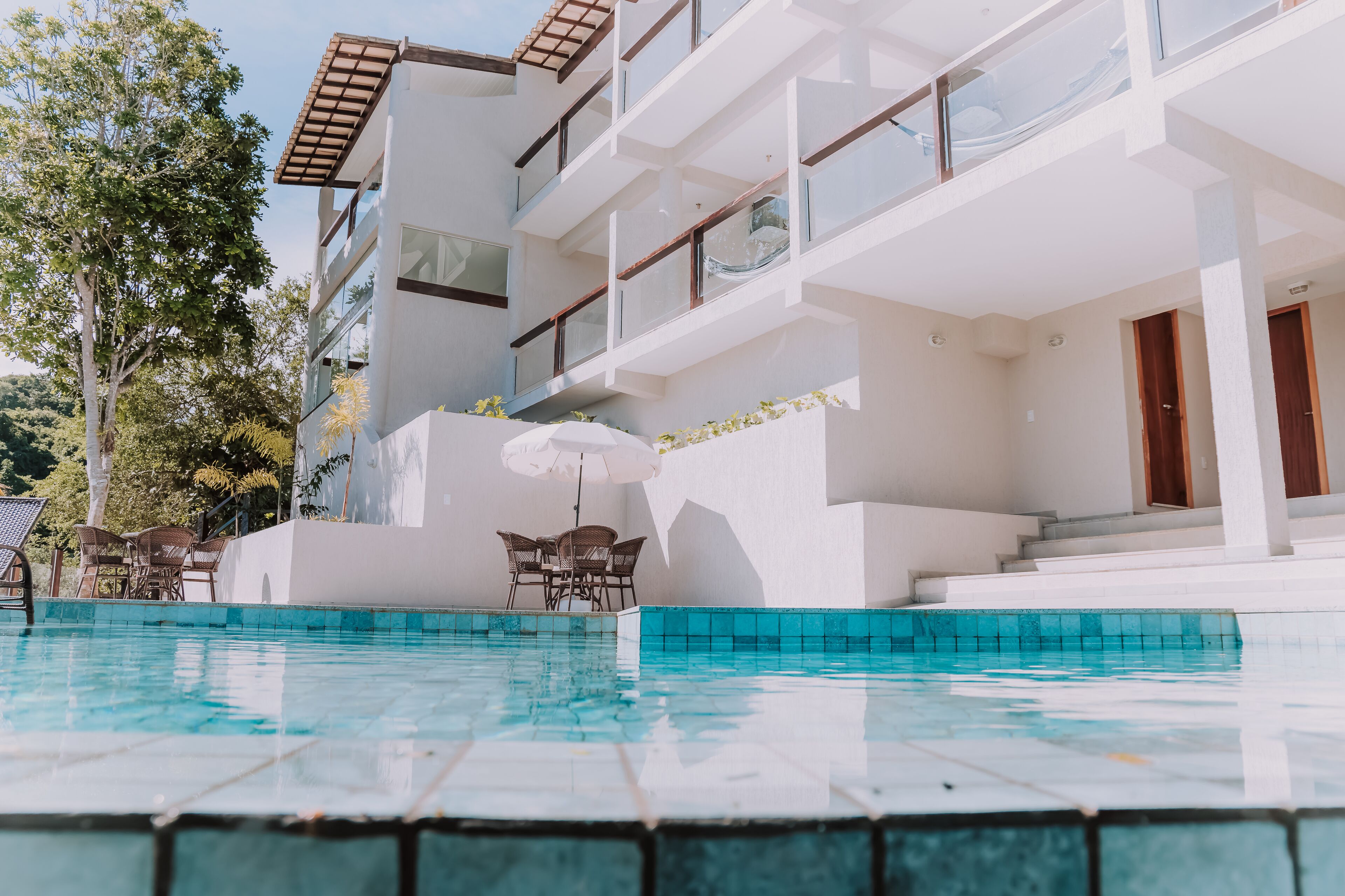 A modern hotel with a swimming pool, outdoor seating, and a multi-story building with balconies.