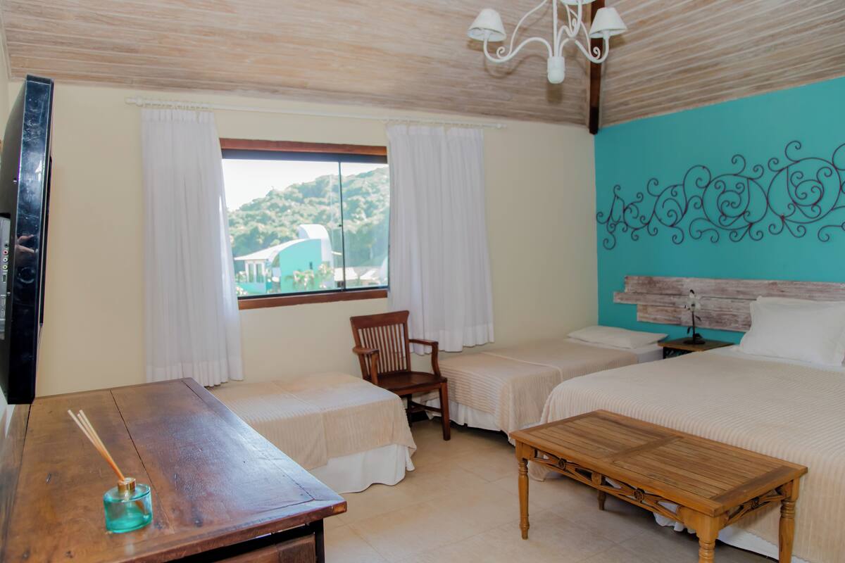 A hotel room with two beds, a wooden table, a chair, and a window with curtains.
