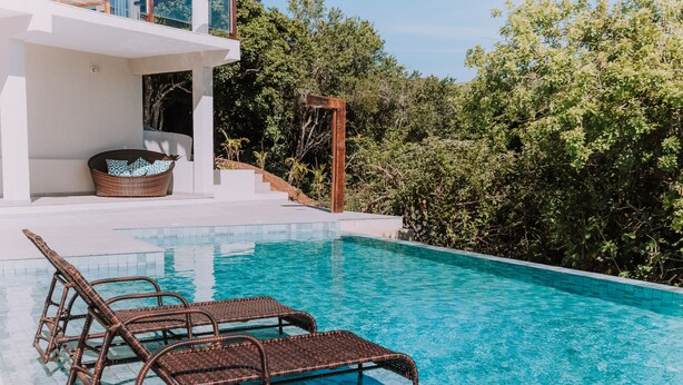 Una piscina moderna al aire libre con sillones de mimbre y un banco blanco.