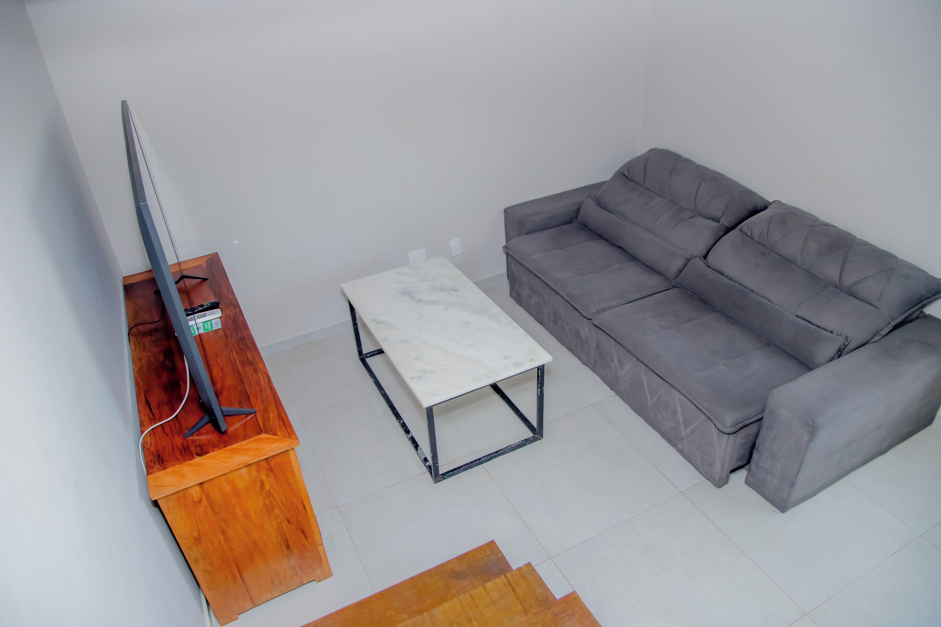 Una sala de estar con un sofá gris, una mesa de centro de madera y un televisor sobre un mueble de madera.