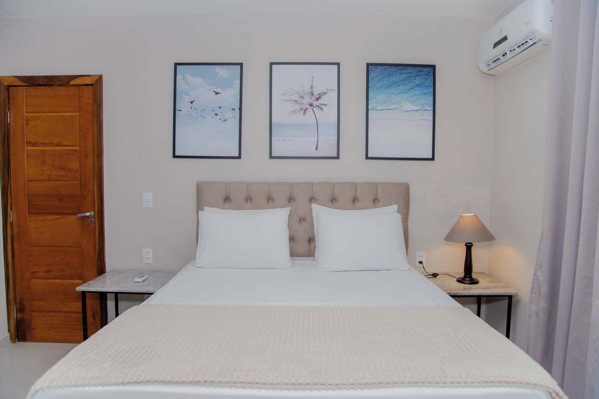 A hotel room with a bed, a nightstand, a lamp, and three framed pictures on the wall.