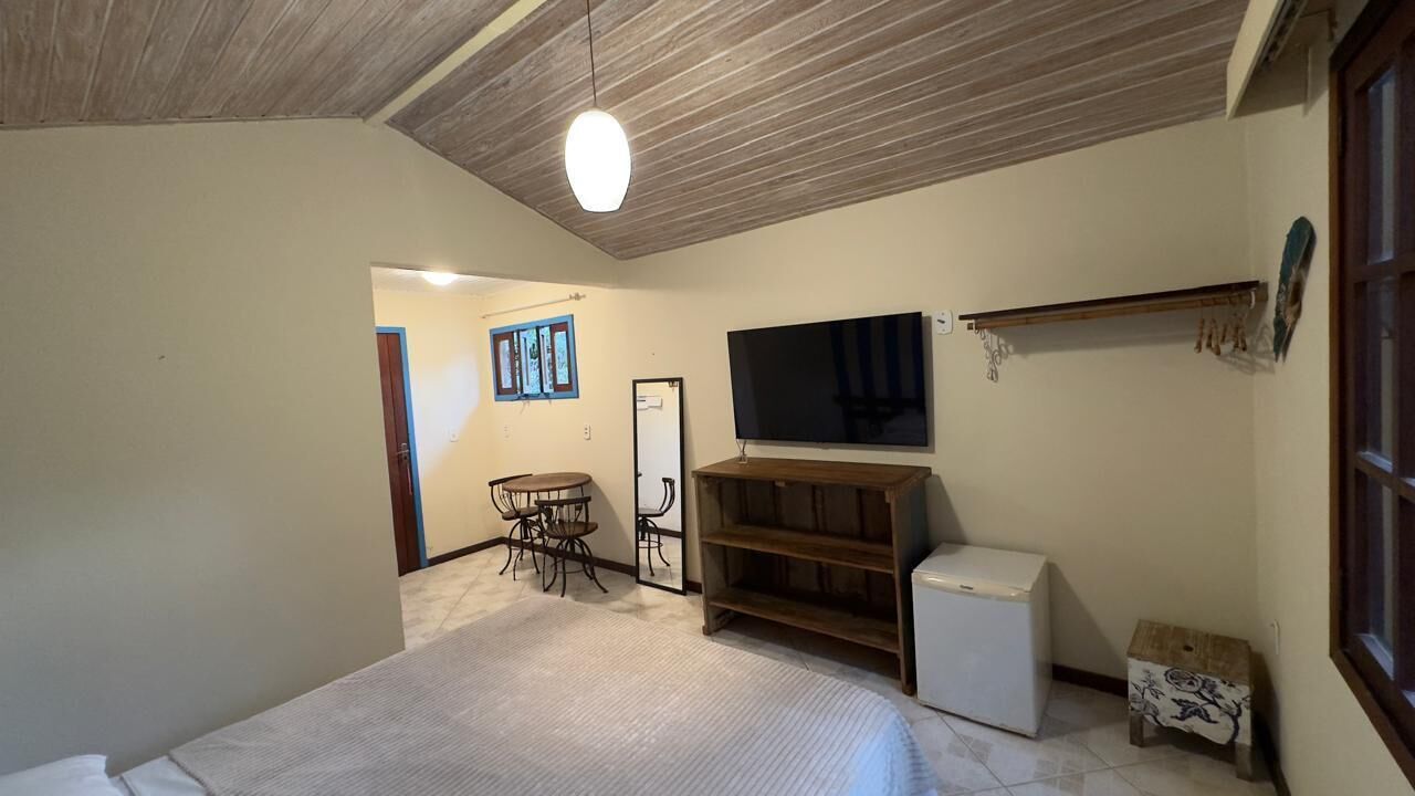 A bedroom with a bed, a TV, a small refrigerator, a wooden shelf, and a chair.