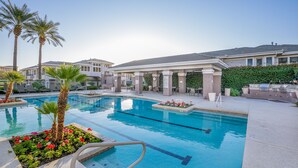 A swimming pool with palm trees and a covered area with chairs and a grill.