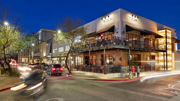 A building with a sign reading "The Mission." It features a ground floor with outdoor seating and a second floor with balconies.