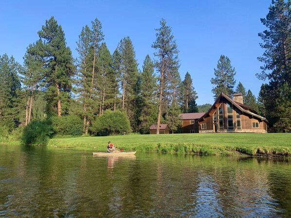 A lodge with a large wooden structure, a pond, and surrounding tall pine trees.