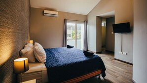 Een slaapkamer met een bed, een bedlamp, een airconditioner, een aan de muur bevestigde televisie en uitzicht op het omliggende landschap door een raam.