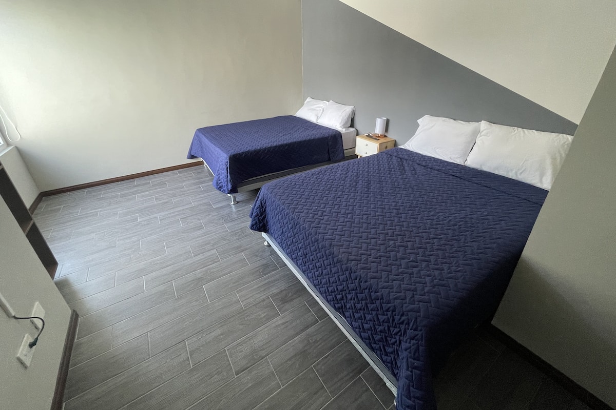 Een hotelkamer met twee bedden, een nachtkastje en een stopcontact op de muur.