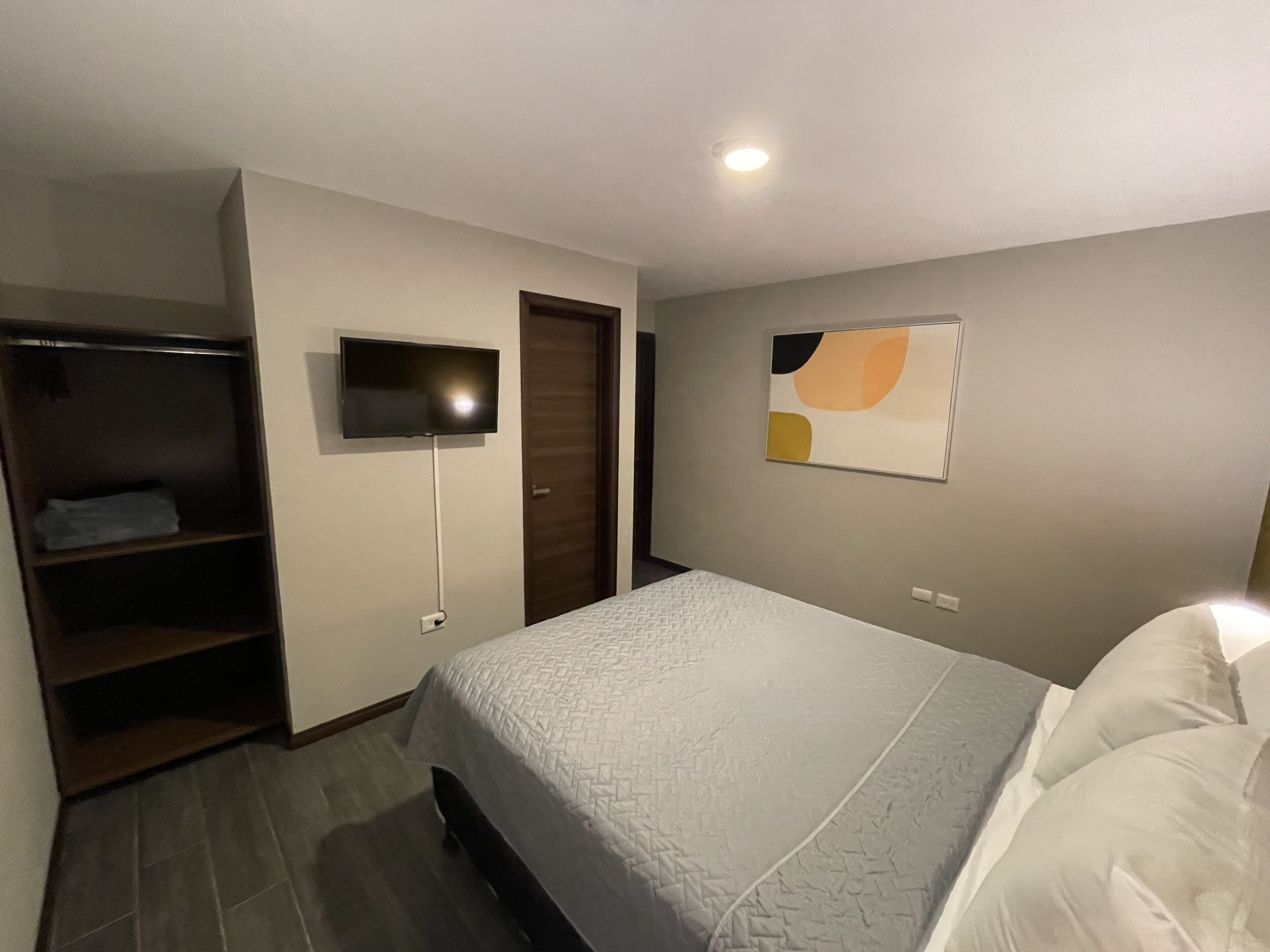 Un dormitorio con cama, televisor montado en la pared, armario y puerta.