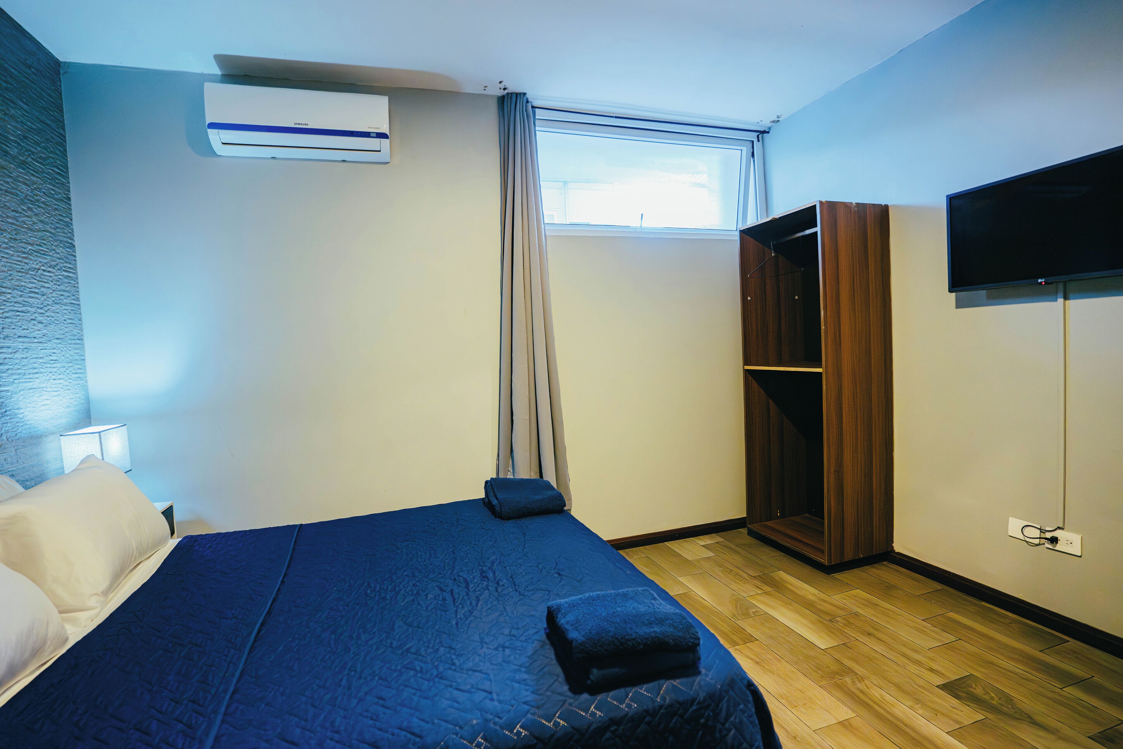 A hotel room with a bed, a wardrobe, a television, and an air conditioning unit.