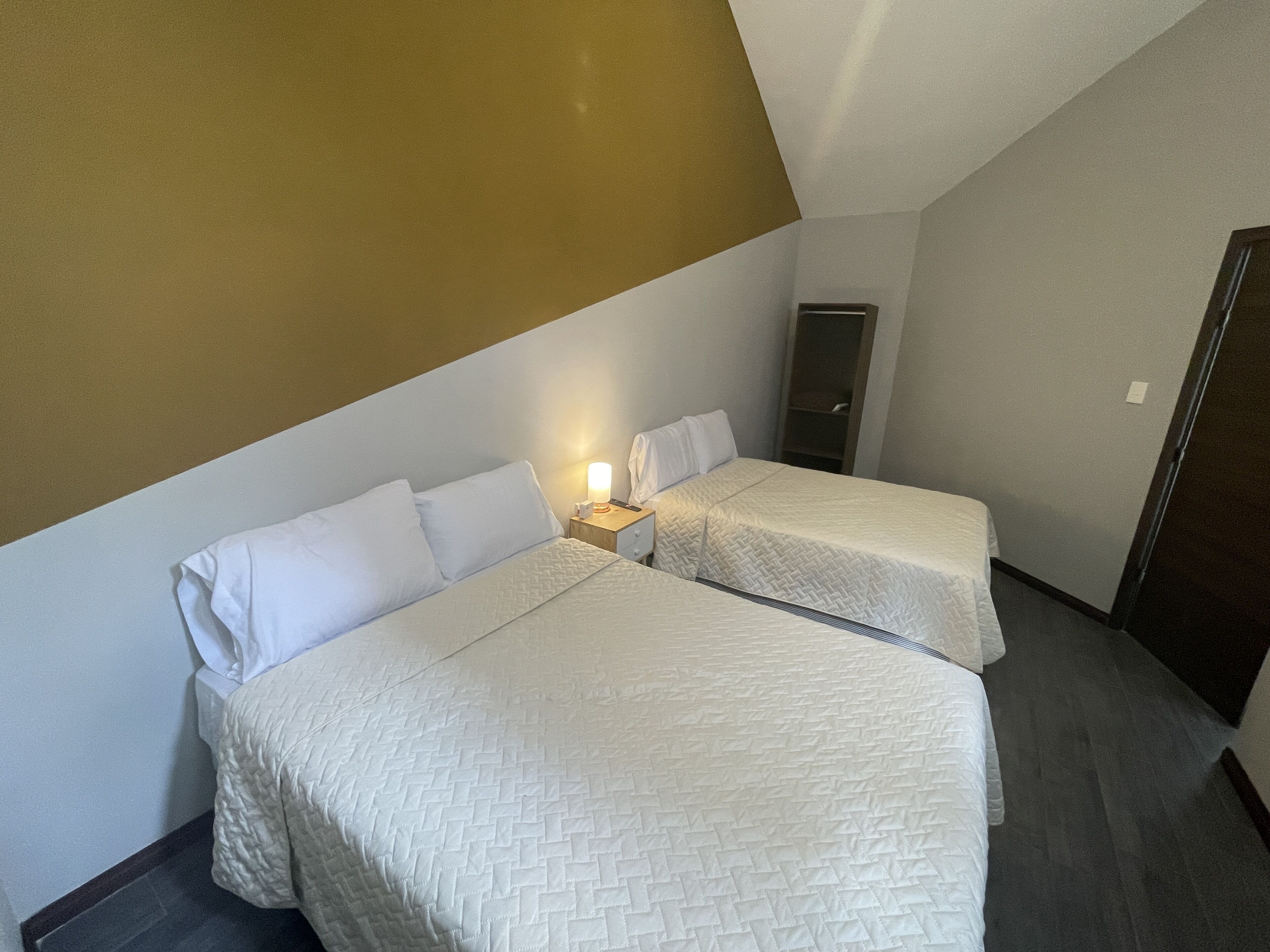 A hotel room with two beds, a nightstand with a lamp, and a wardrobe.