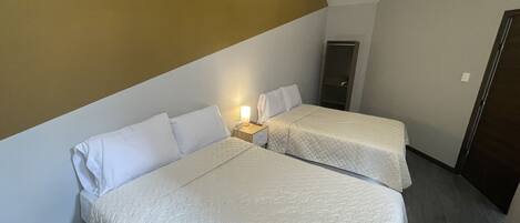 A hotel room with two beds, a nightstand with a lamp, and a wardrobe.