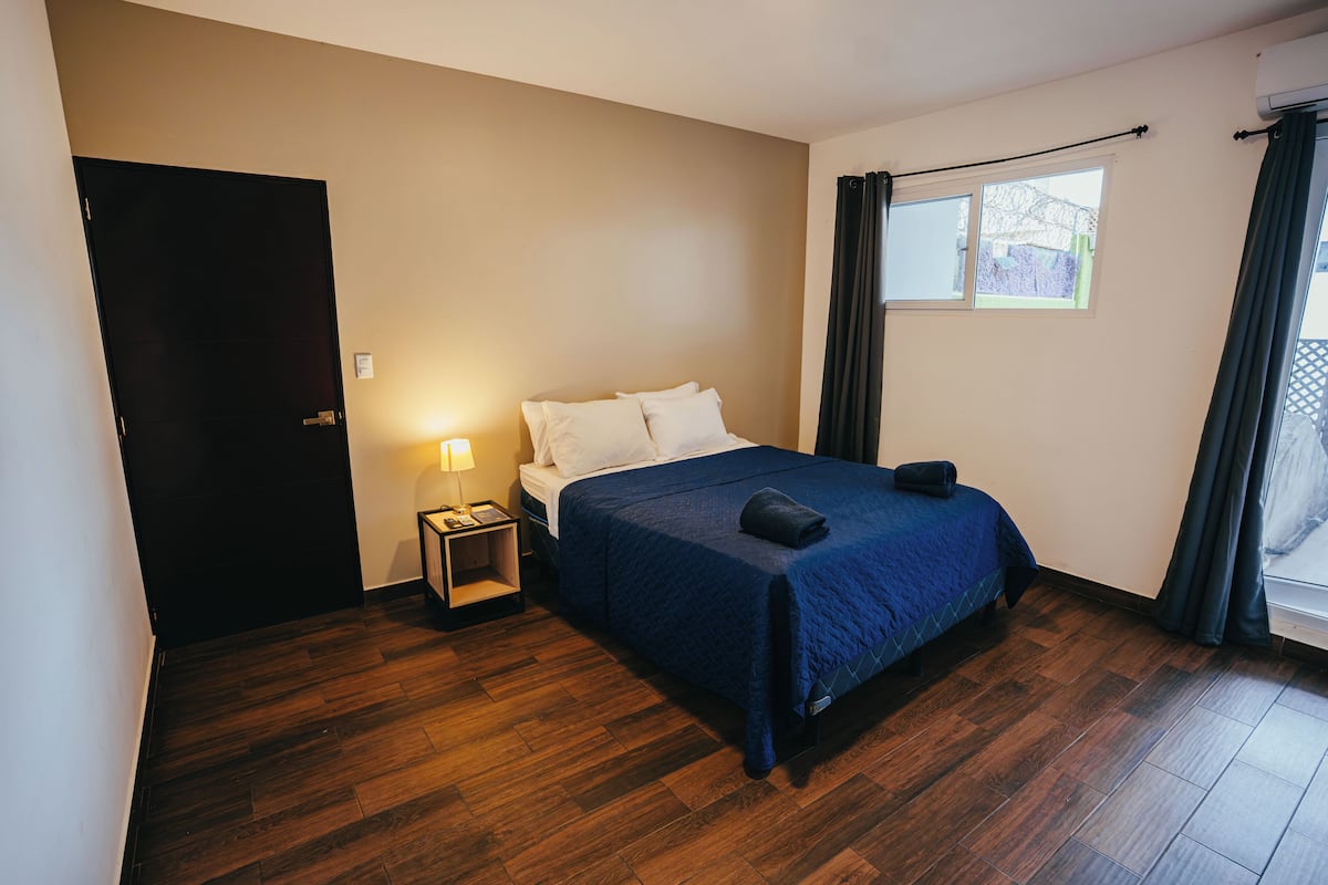 Een slaapkamer met een bed, nachtkastje, raam en deur.