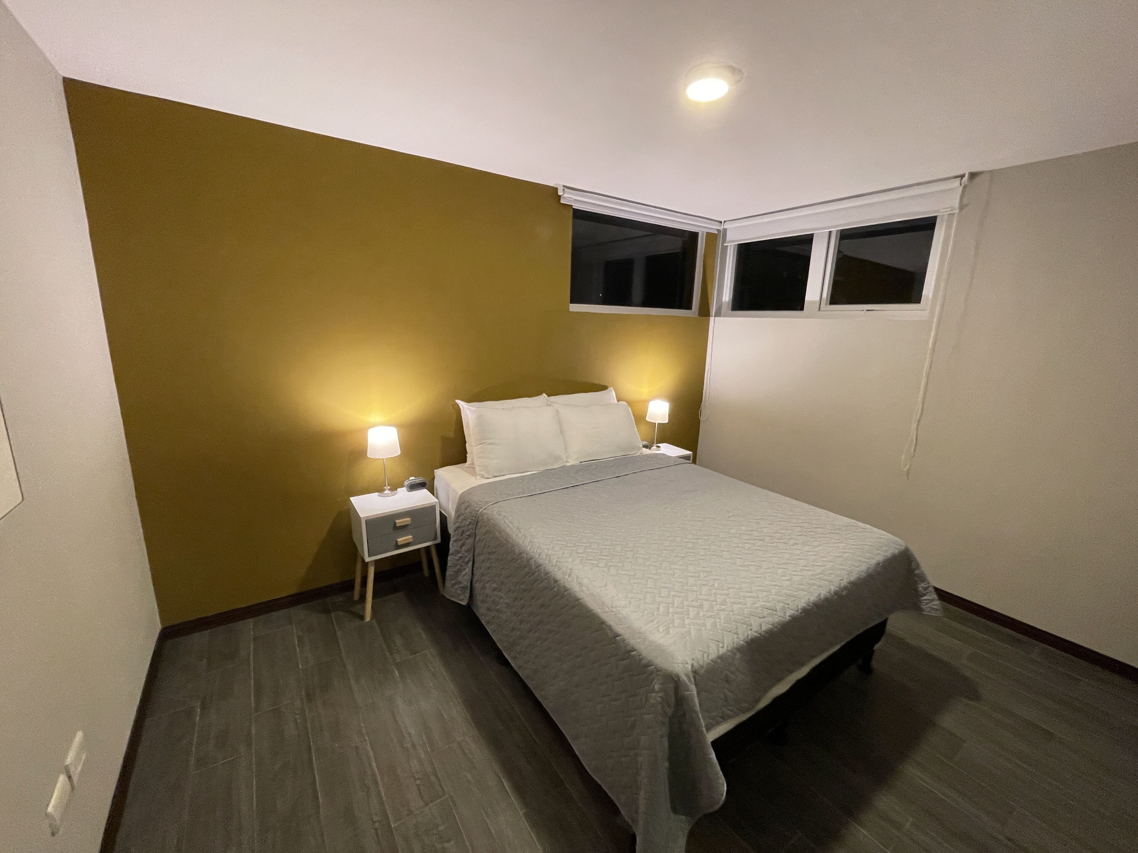 Uma cama de solteiro com colcha cinza em um quarto com parede de destaque marrom e uma janela.