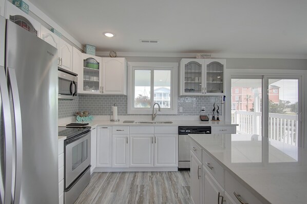 A modern kitchen with white cabinetry, a stainless steel refrigerator, a built-in oven, and a dishwasher. - Home on a deep water canal -private dock- 4 min walk to the beach- endless views (Holden Beach)