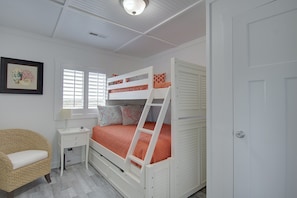 A bunk bed with a ladder, a white desk, a wicker chair, and a framed picture on the wall.