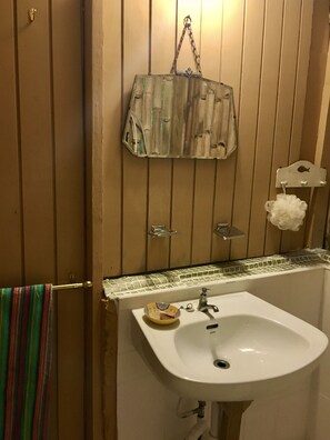 A bathroom with a wooden panel wall, a white sink, a hanging bag, and a towel rack with a colorful towel. - Secluded self contained cabin close to Blue lagoon (Zion Hill)