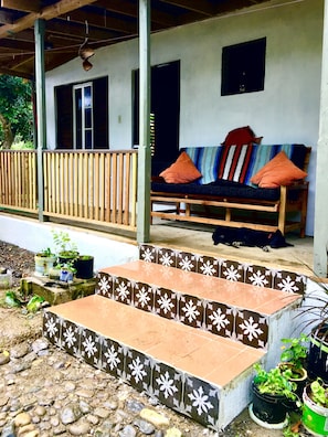 Een veranda met een houten bankje, trappen met een betegeld patroon en bloempotten.
