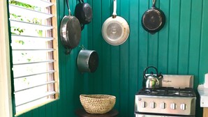 Cocina compacta con estufa a gas, bombona y diferentes ollas y sartenes colgadas en la pared.