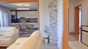 Ein modernes Wohnzimmer mit einer Couch, einer Essecke mit Stühlen und einem Tisch, und einer Küche im Hintergrund.