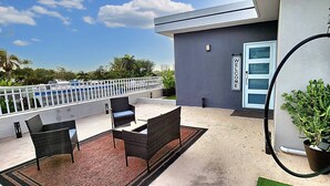 Un balcon avec des meubles en osier, une plante en pot et une pancarte « BIENVENUE » sur un bâtiment.