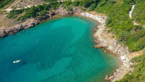 An aerial view of a coastal area with a clear turquoise bay, rocky shoreline, and a path leading to a beach with umbrellas. - Vacation home Matea by Interhome (Krk/Dobrinj)