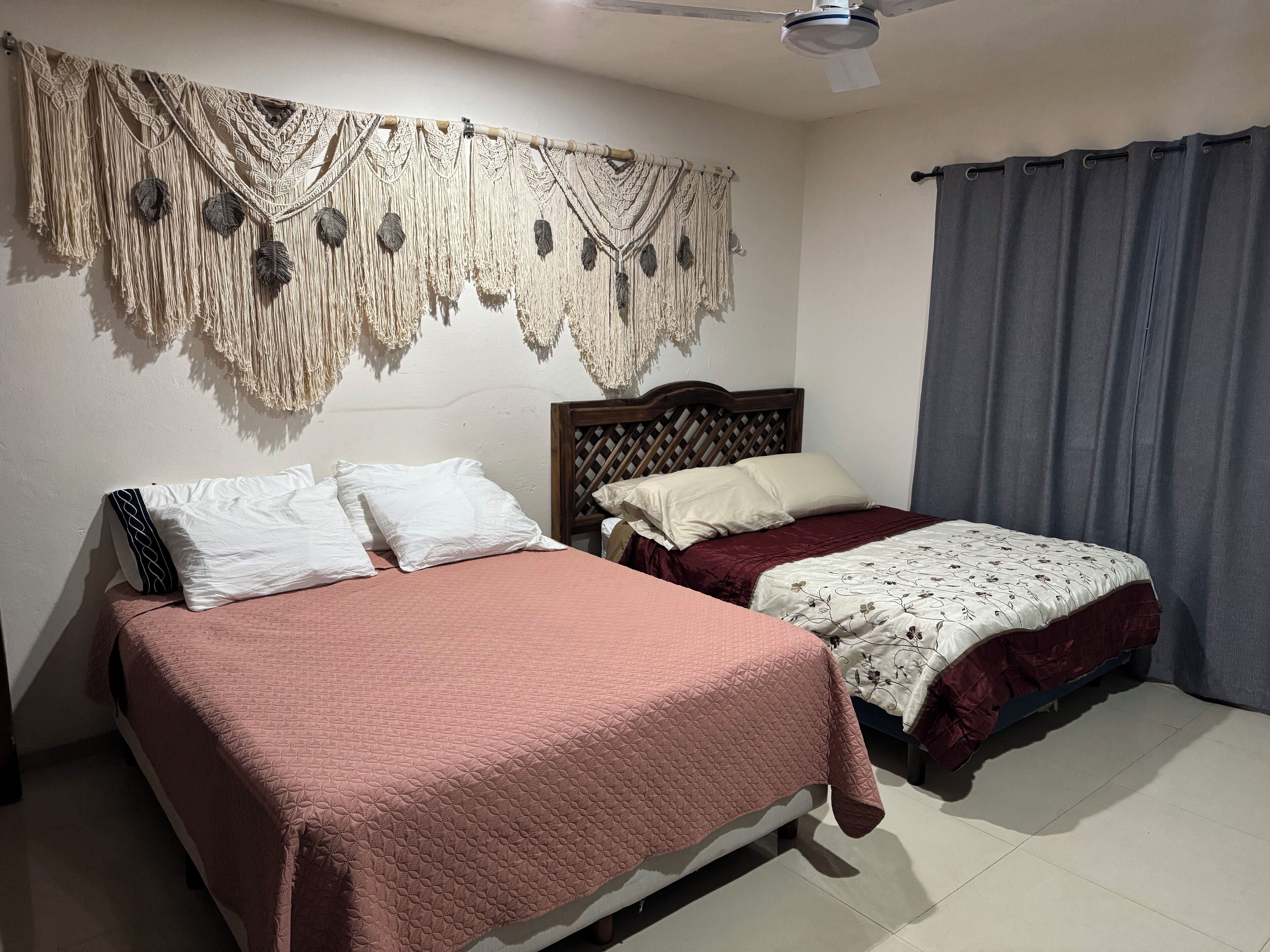 Een slaapkamer met twee bedden, een macramé wanddecoratie en een plafondventilator.