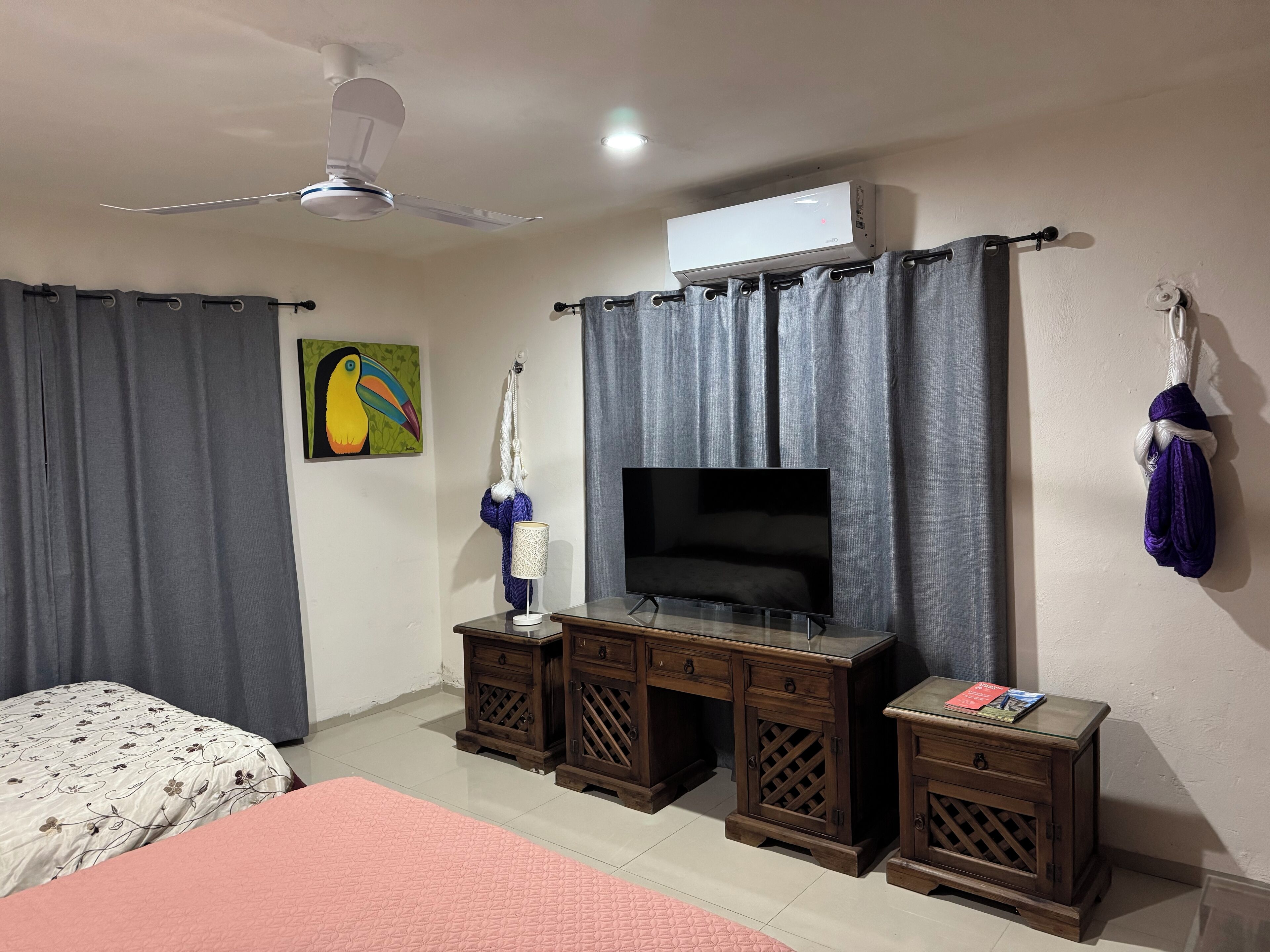 A bedroom with a bed, a TV, wooden nightstands, a ceiling fan, and a window with curtains.