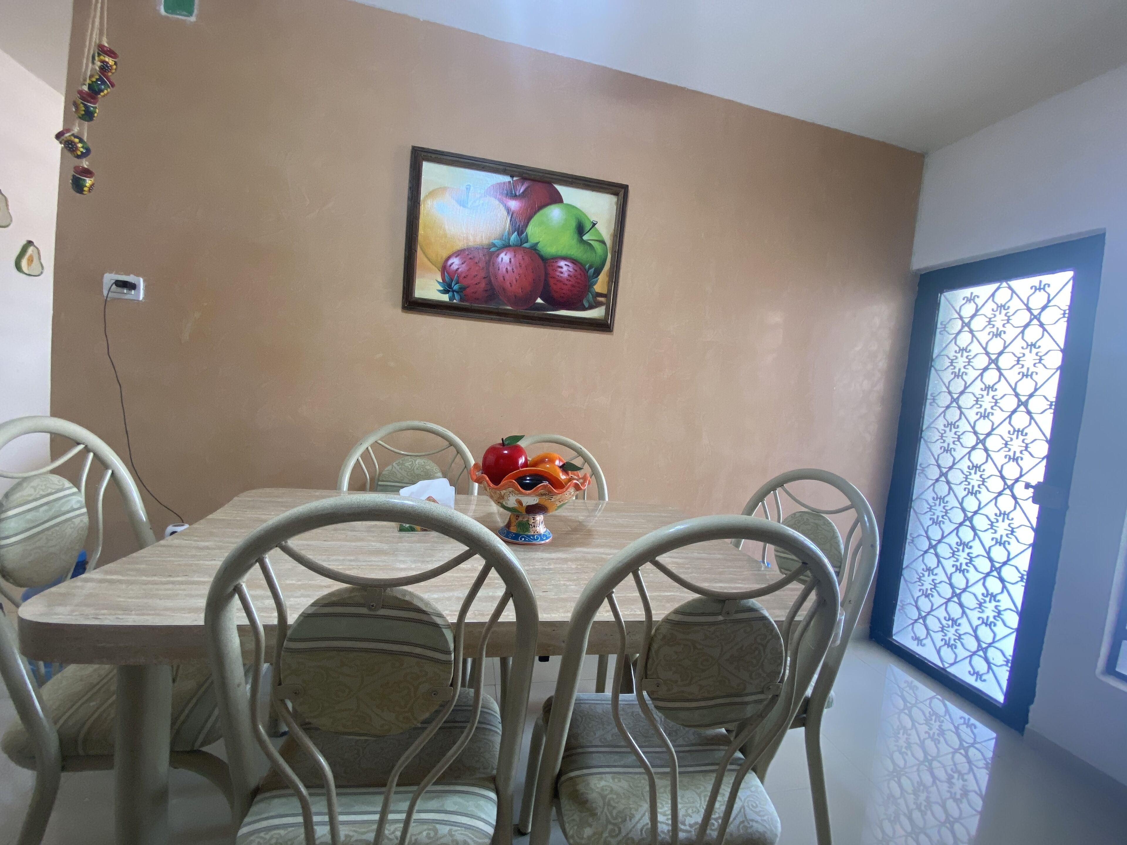Een eethoek met een tafel, stoelen, een fruitschaal en een aan de muur hangend schilderij.