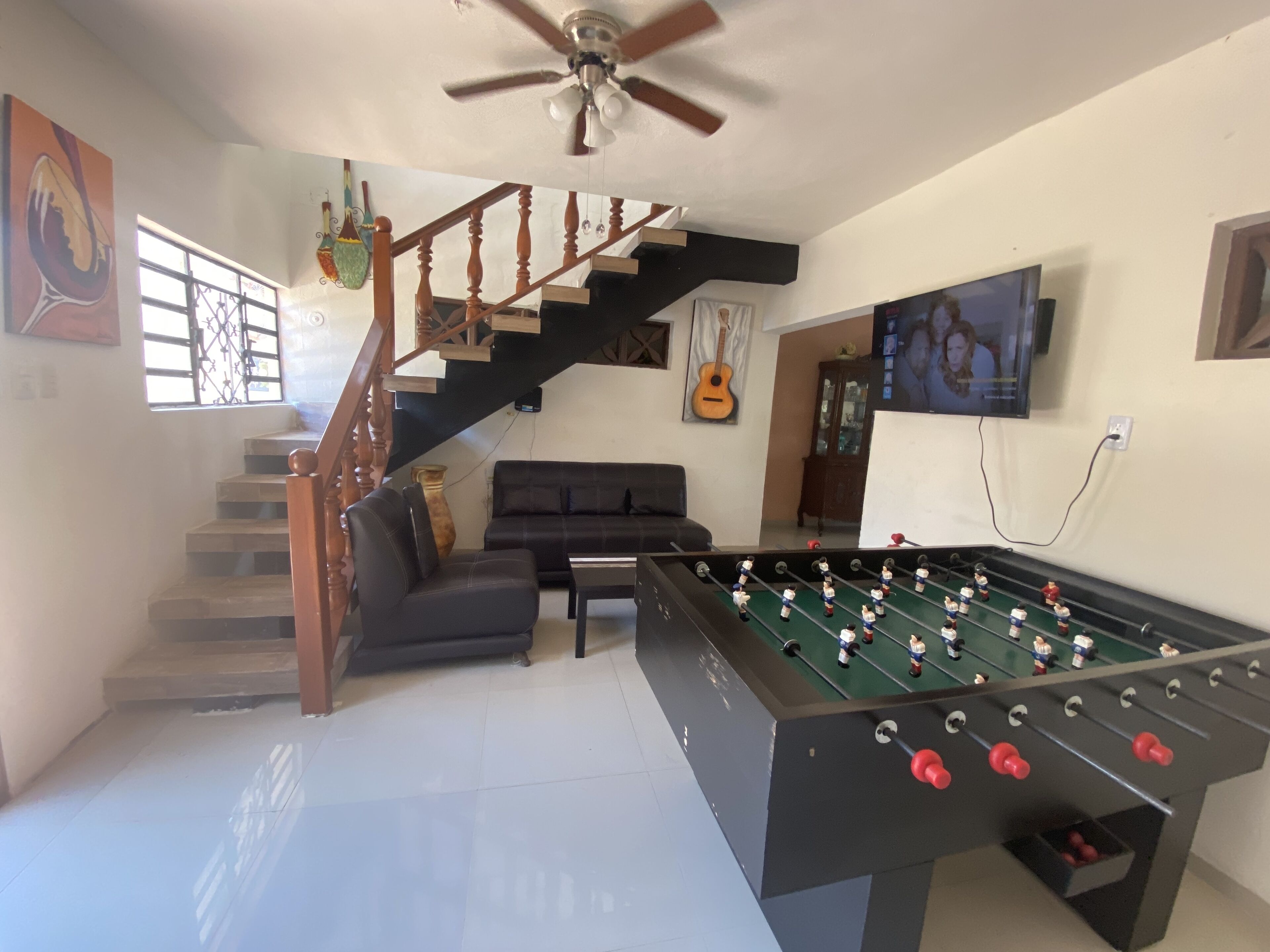 A living room with a foosball table, a sofa, a staircase, and a television.