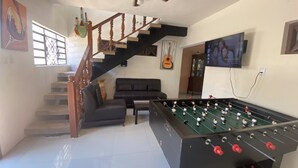 A living room with a foosball table, a sofa, a staircase, and a television. - 300MB/S Wifi with an amazing pool 3 Bed 2.5bath house (Mérida)