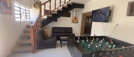 A living room with a foosball table, a sofa, a staircase, and a television.