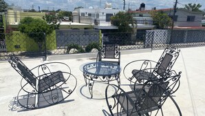 A patio with metal chairs and a table, surrounded by a low fence and buildings in the background. - 300MB/S Wifi with an amazing pool 3 Bed 2.5bath house (Mérida)
