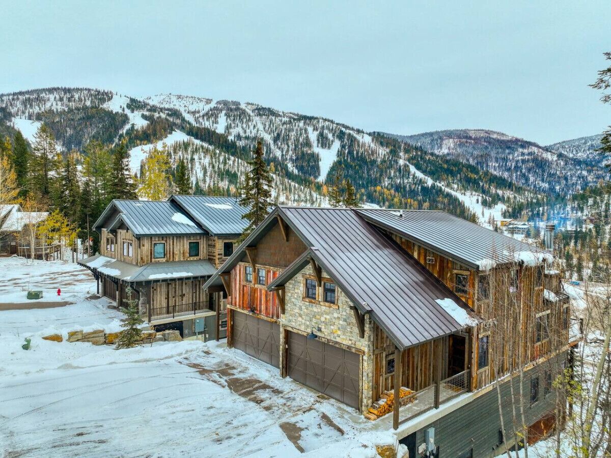 Una hilera de edificios de estilo cabaña de troncos con techos metálicos, rodeados de montañas y árboles cubiertos de nieve.