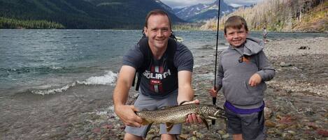 Two people holding a fish by a river with mountains in the background.