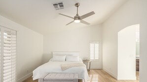 Ein Schlafzimmer mit einem Bett, einem Deckenventilator, einem Fenster mit Jalousien und einem Holzboden.