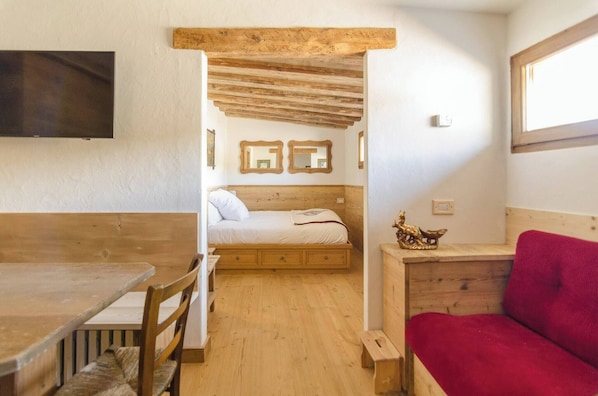 Une pièce avec un lit en bois, un canapé rouge, une table en bois et un téléviseur fixé au mur.