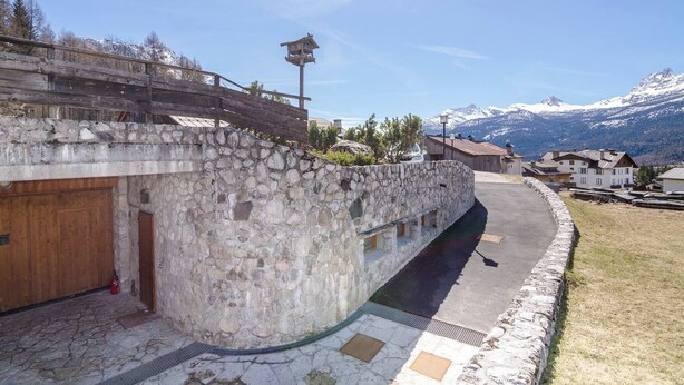 A stone building with a wooden door, a stone wall, and a view of mountains. - Tofana Cosy Studio - 2 persons (Cortina d´Ampezzo)