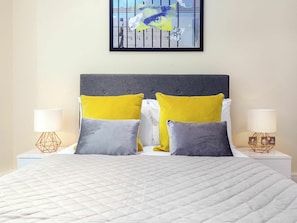 A neatly made bed with a quilted white duvet, two bedside tables with lamps, and a framed abstract painting above the bed.