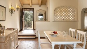 Un coin repas avec une table blanche dressée pour quatre personnes, un banc et une vue sur l’extérieur par une fenêtre ornée d’un motif en treillis.