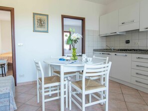 A small, bright kitchen with white cabinets and a dining area with a white table and chairs.