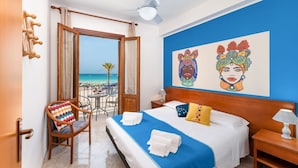 Une chambre d’hôtel avec un lit, une chaise, une table de chevet, un ventilateur de plafond et une vue sur la plage.