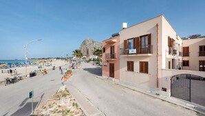 Une rue côtière bordée d’immeubles, avec une plage et une montagne en arrière-plan.