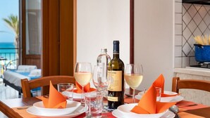 Une table à manger dressée avec des assiettes, des verres et une bouteille de vin, avec une vue sur la mer et une piscine en arrière-plan.