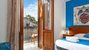 A hotel room with a bed, a nightstand, a blue wall, and a view of the outside. - Beach Apartments - Two-Room (San Vito Lo Capo)