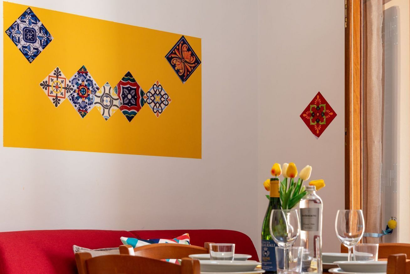 A dining area with a yellow wall, a red sofa, and a table set with plates, glasses, and a bottle of water.