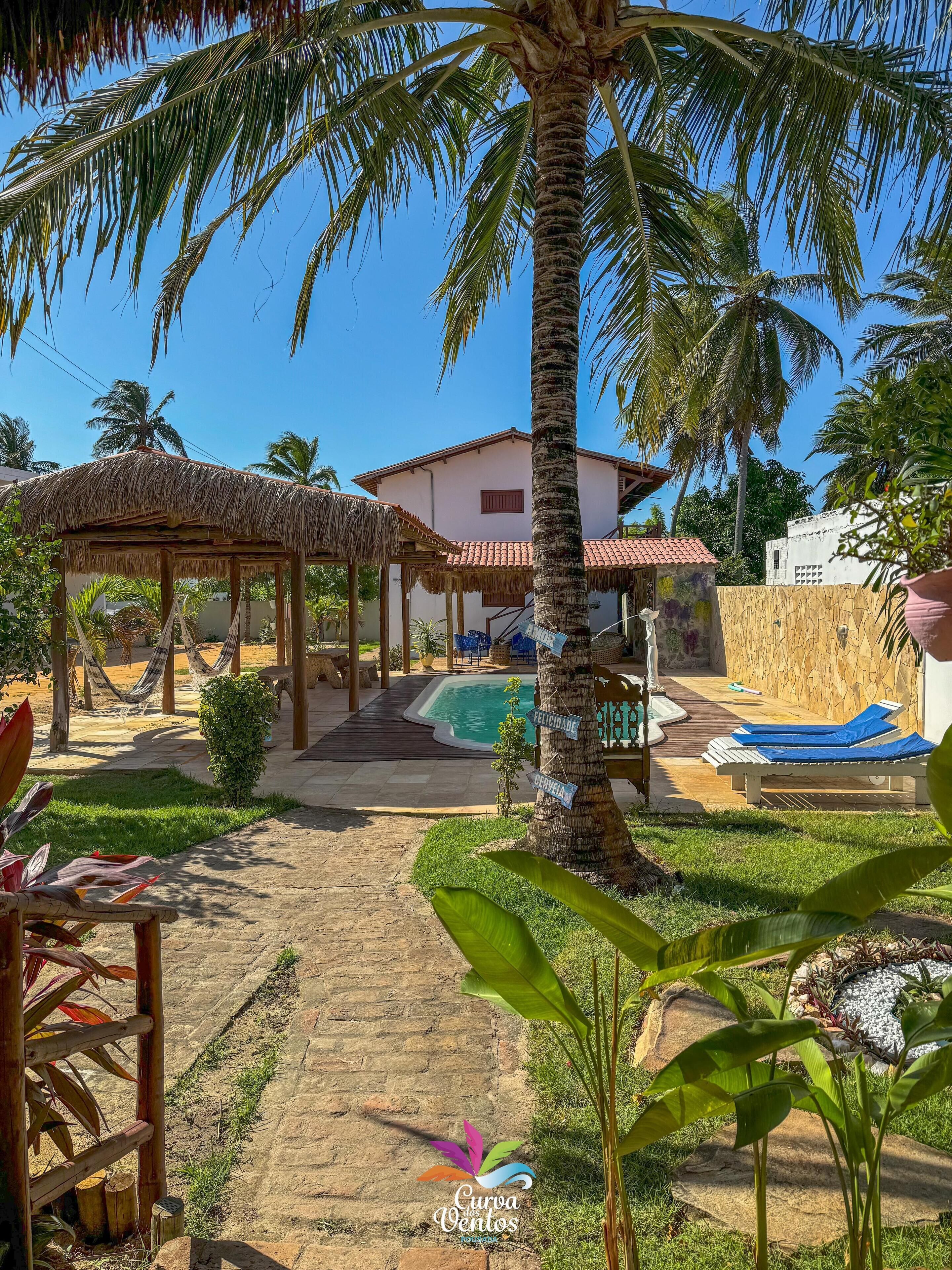 A pool area with lounge chairs, a thatched-roof structure, and a palm tree.