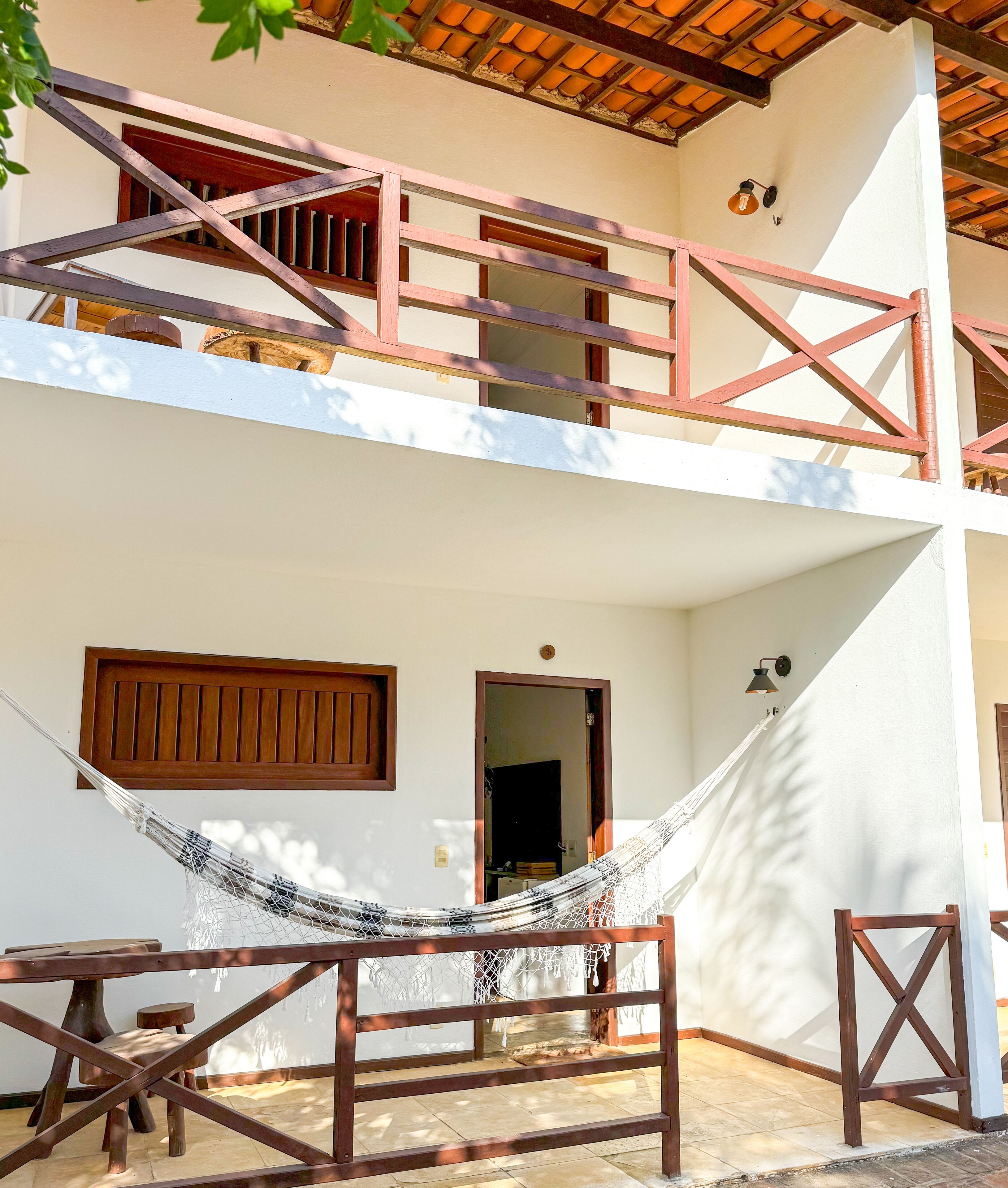 A two-story building with a wooden balcony, a hammock, and a wooden table.